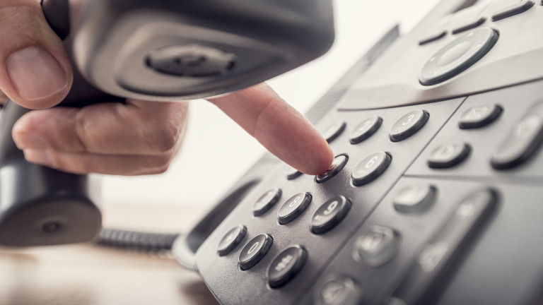 Closeup of male hand holding telephone receiver while dialing a