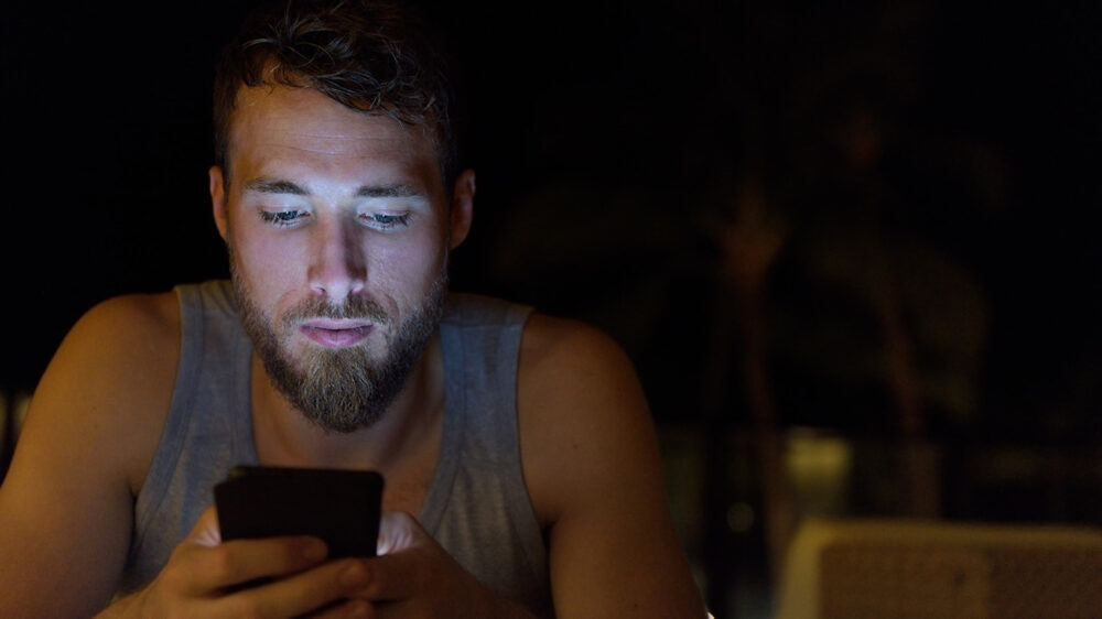 Man using smartphone at night browsing internet updating social