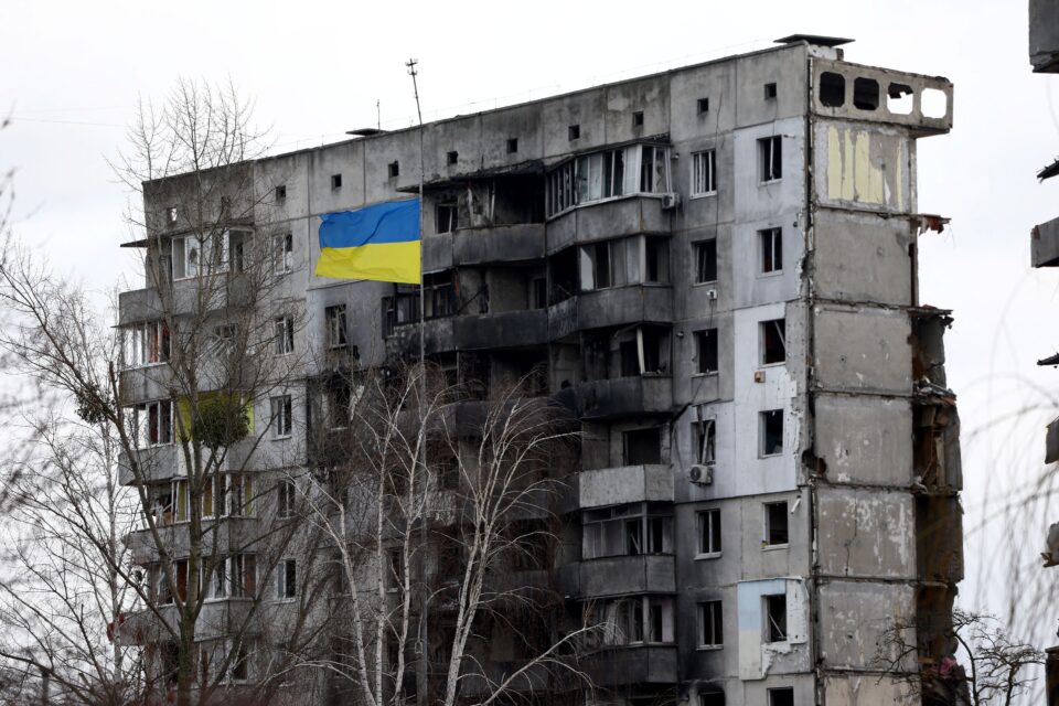A Ukrainian national flag flies in front of a destroyed residential building in Borodianka