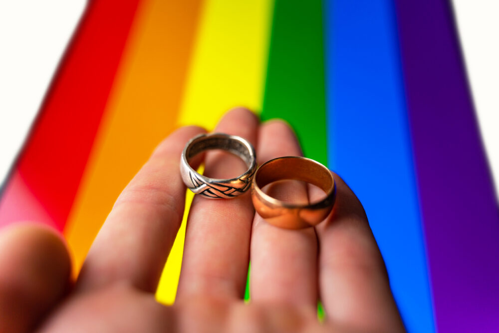 Gay wedding proposal. hand holds two wedding rings on lgbt flag background. same sex marriage, homosexuality and legalized relationship of two lgbt people