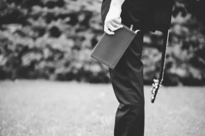 Grayscale shot male holding bible guitar his back